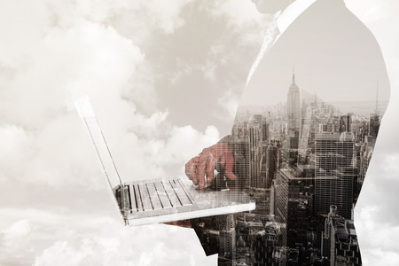 Businessman holding laptop against new york skylineの写真素材