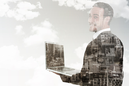 Businessman looking at camera holding laptop against new york skylineの写真素材