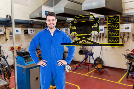 Smiling mechanic with hands on hips standing by tire against workshopの写真素材