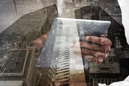 Businessman scrolling on his digital tablet against low angle view of skyscrapersの写真素材