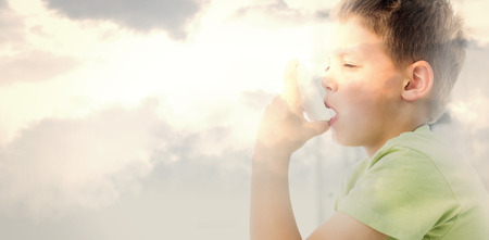 Boy using an asthma inhaler in clinic against grey cloudy skyの写真素材