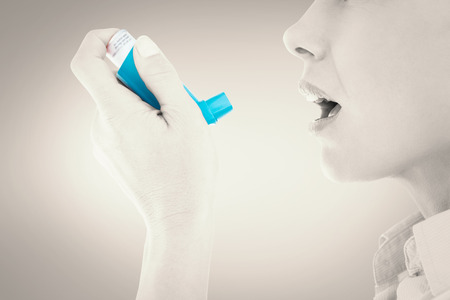 Close up of a woman using an asthma inhaler against grey vignetteの写真素材