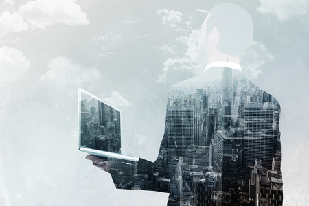 Businessman looking up holding laptop against new york skylineの写真素材
