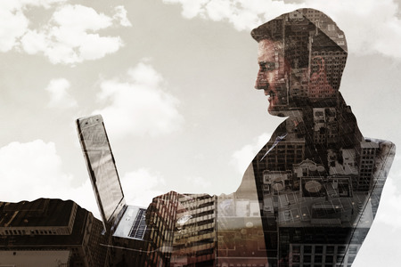 Businessman using laptop against low angle view of skyscrapersの写真素材
