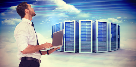 Sophisticated businessman standing using a laptop  against composite image of server towers