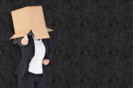 Businesswoman showing thumbs up with box over head against grey backgroundの写真素材