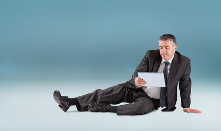 Mature businessman sitting using tablet against blue vignette backgroundの写真素材