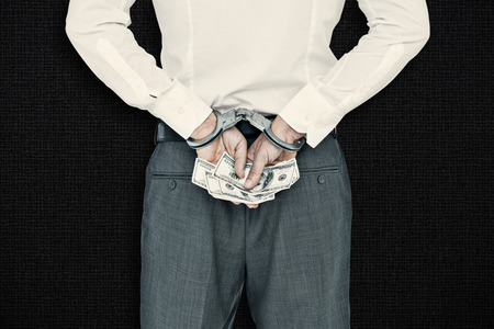 Businessman in handcuffs holding bribe against black backgroundの写真素材