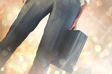 Businessman holding briefcase against yellow abstract light spot designの写真素材