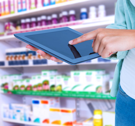 Woman using tablet pc  against close up of shelves of drugsの写真素材