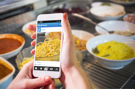 Hand holding smartphone against delicious bowls of fresh salads