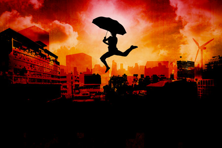Woman jumping with umbrella against artistic cityscape designの写真素材