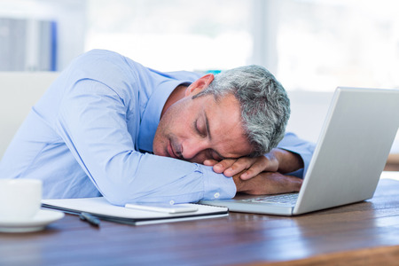 Businessman sleeping on laptop computer in officeの写真素材
