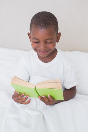 Pretty little boy reading in bed at home in bedroomの写真素材