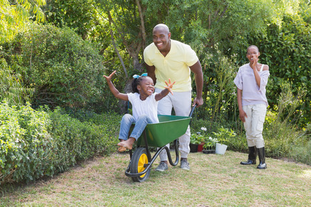 Happy smiling couple playing with wheelbarrow and their daughter at home in garden
