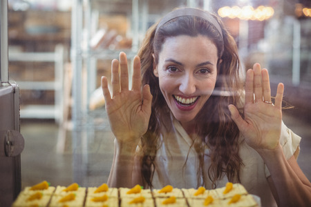 Pretty brunette looking at pastries through the glass in the bakery storeの写真素材