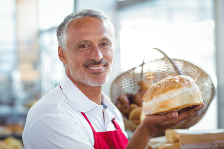 Waiter looking at camera and holding freshly baked bread in the bakeryの写真素材