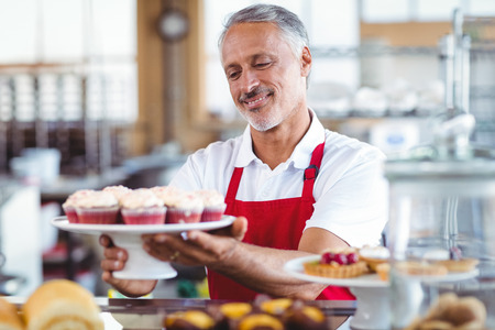 Happy barista holding a plate of cupcakes in the bakeryの写真素材