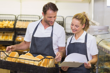Smiling bakers looking at notepad and holding a basket with bread in bakery