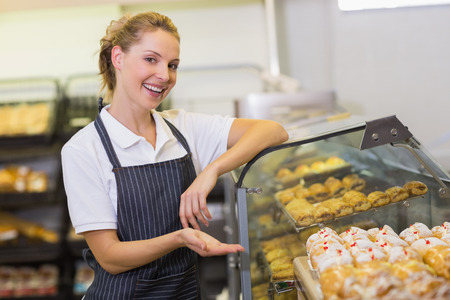 Portrait of a smiling blonde baker showing a pastry in bakeryの写真素材