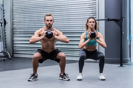 Kneeling muscular couple exercising with kettlebellsの写真素材