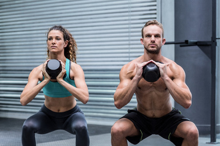 Kneeling muscular couple exercising with kettlebellsの写真素材