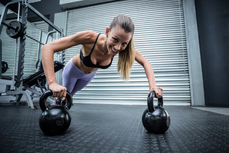 Portrait of muscular woman doing pushups with kettlebells