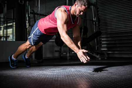 Muscular man doing push-ups with hand clapping in crossfit gym