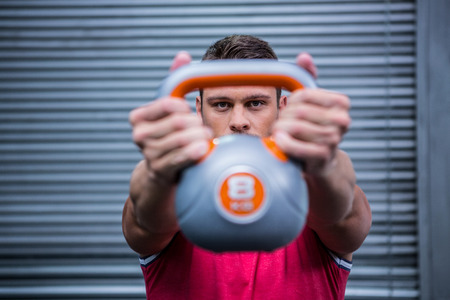Muscular man lifting a kettlebell in crossfit gym