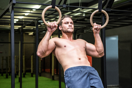 Muscular man doing ring gymnastics in crossfit gym