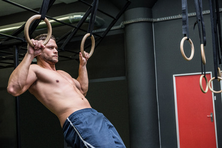 Muscular man doing ring gymnastics in crossfit gym