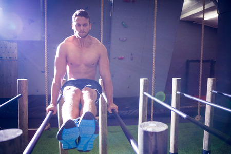 Muscular man exercising on parallel bars in crossfit gym
