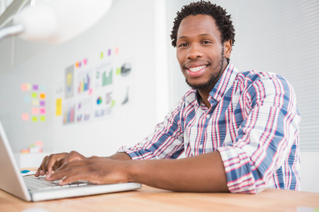 Young businessman types on the laptop and looks at the camera in the officeの写真素材
