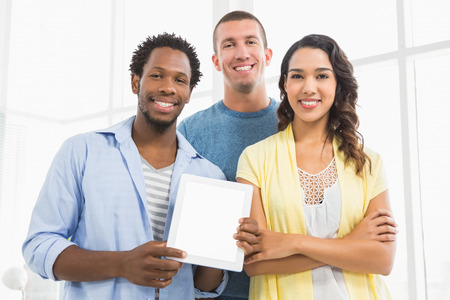 Portrait of smiling colleagues presenting tablet computer and looking at camera in the officeの写真素材
