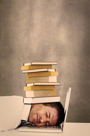 Tired businessman resting on laptop against grey roomの写真素材