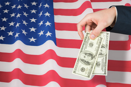 Hand holding hundred dollar bills against rippled us flag