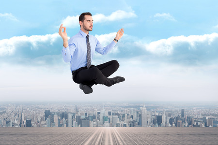 Relaxed businessman sitting in lotus pose against city on the horizonの写真素材