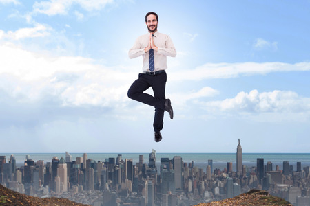 Smiling businessman standing in tree pose against large city on the horizonの写真素材