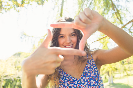Pretty brunette doing frame with her fingers on a sunny dayの写真素材