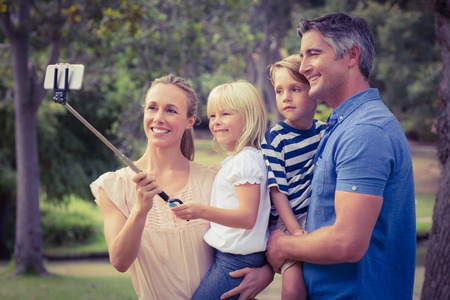 Happy family using a selfie stick in the park on a sunny dayの写真素材