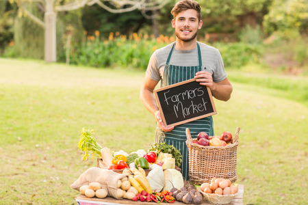 Handsome farmer standing at his stall and holding chalkboard on a sunny dayの写真素材