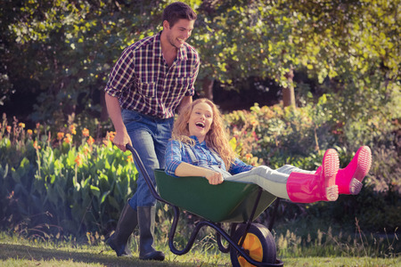 Man pushing his girlfriend in a wheelbarrow on a sunny dayの写真素材