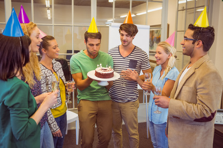 Businessman blowing candles on her birthday cake in the office Businessman blowing candles on her birthday cake in the office