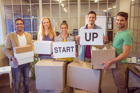 Portrait of young creative business people holding cardboard written start upの写真素材