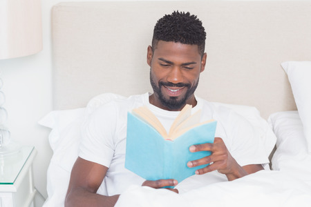Handsome man reading in bed at home in bedroomの写真素材