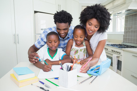 Happy parents helping children with homework at home in the kitchenの写真素材