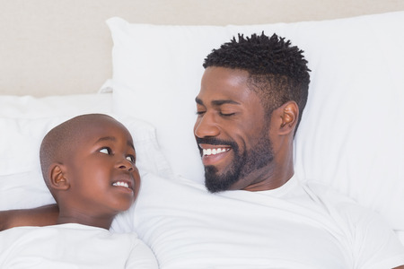 Father and son smiling at each other at home in bedroomの写真素材