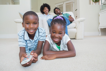 Happy siblings lying on the floor watching tv at home in the living roomの写真素材