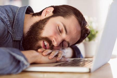 Hipster businessman sleeping at his desk in his officeの写真素材