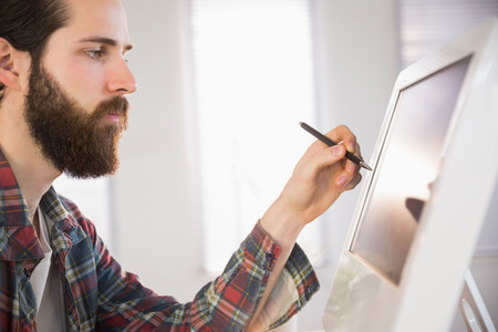 Hipster businessman pointing at computer with pen in his officeの写真素材